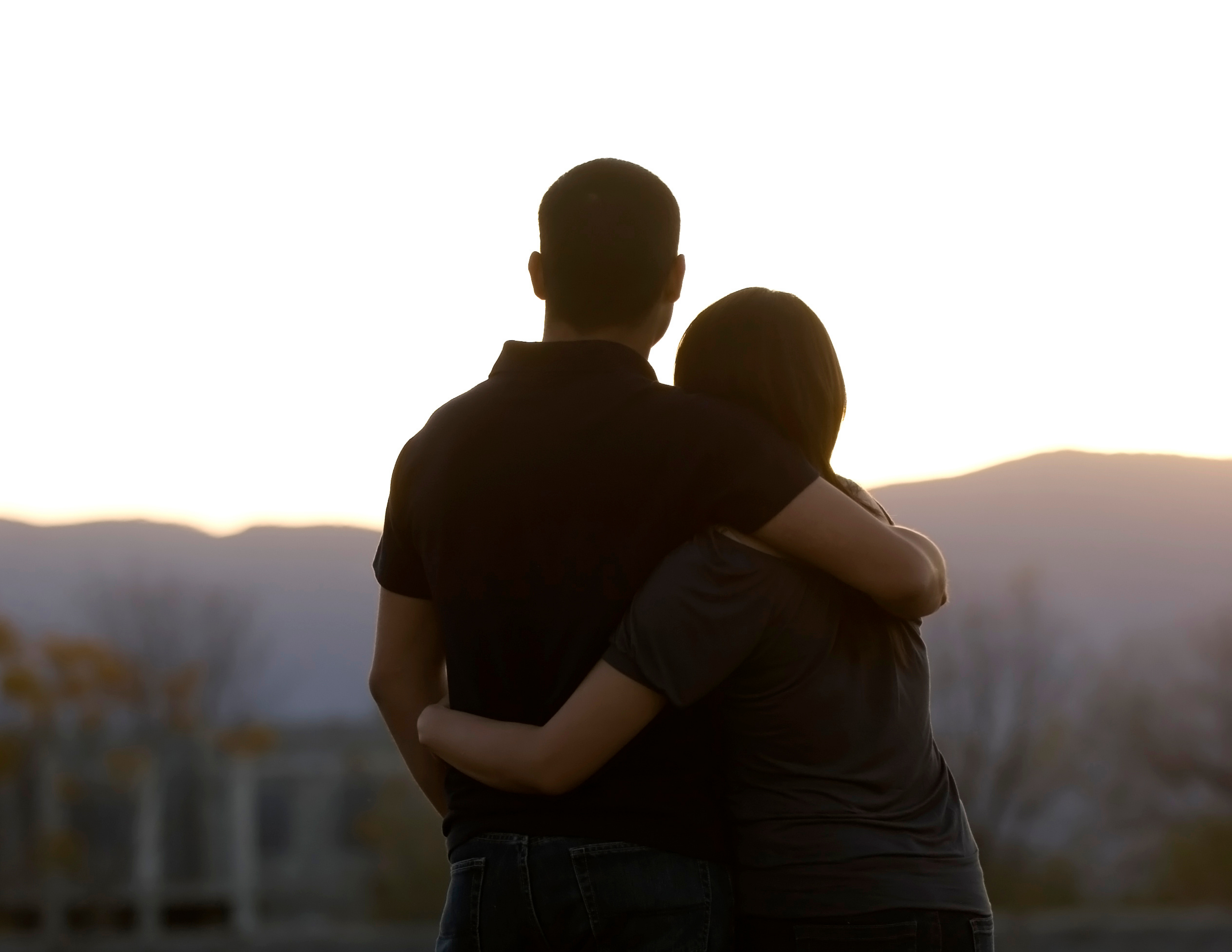 Woman and man look towards mountains, with backs turned to camera and arms around each other.